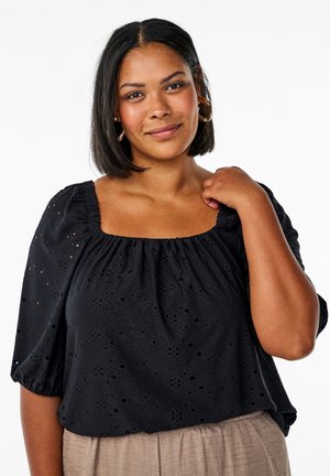 Črna bluzica s kvadratnim izrezom, kratkimi nabranimi rokavi in broderie anglaise teksturo. Uparjena s svetlo rjavimi teksturiranimi hlačami.