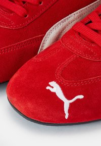 Gros plan de baskets Puma en suède rouge avec des lacets rouges et le logo blanc Puma sur la zone des orteils.