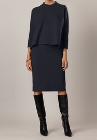 Completo due pezzi blu navy composto da una maglia a maniche lunghe ampia e rigata e una gonna aderente fino al ginocchio, abbinato a stivali neri alti fino al ginocchio.