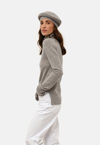 Šedý pletený svetr s vysokým límcem a žebrovanými manžetami, spárovaný s bílými kalhotami širokého střihu. Oblečení doplňuje odpovídající šedý baret.