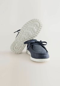 Marineblaue Segelschuhe aus Canvas mit strukturiertem Finish, weißer Gummisohle und passenden Schnürsenkeln. Rundliche Form mit minimalen Nähdetails.