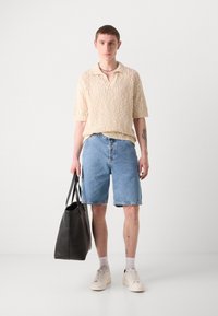 Beige strikket polo skjorte, denimshorts, svart totebag, hvite joggesko og grå sokker. Enkle, avslappede, uformelle klesplagg.