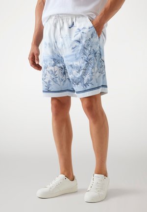 Zwemshorts in lichtblauw met een palmbomenprint, elastische tailleband, zijzakken en contrasterende donkerblauwe zoom. Gecombineerd met witte sneakers.