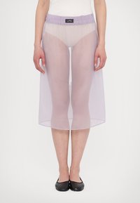 Läpinäkyvä, lavendelfärgad midikjol med elastisk midja, knälång, med sprund fram, i kombination med en vit topp och svarta platta skor. Minimalistisk design.