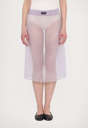 Przezroczysta, lawendowa spódnica do talii z elastycznym paskiem, o długości do kolan, z rozcięciem z przodu, zestawiona z białą bluzką i czarnymi balerinami. Minimalistyczny design.