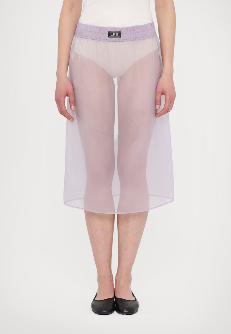 Läpinäkyvä, lavendelfärgad midikjol med elastisk midja, knälång, med sprund fram, i kombination med en vit topp och svarta platta skor. Minimalistisk design.