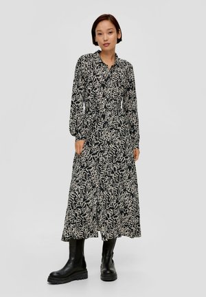 Longue robe noire avec un motif floral abstrait blanc, fermeture à boutons et manches longues ; associée à des bottes noires jusqu'aux genoux.
