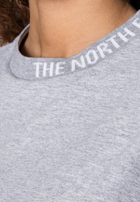 Grå sweatshirt med rundad halsringning, med en ribbad krage som har vit text som säger "THE NORTH FACE" längs kanten.