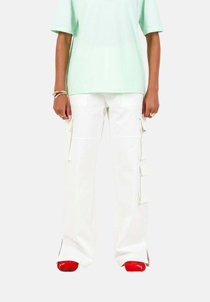 Pantalons cargo blancs avec poches latérales, couture détaillée et fentes à l'ourlet, associés à un t-shirt vert menthe et des baskets rouges.