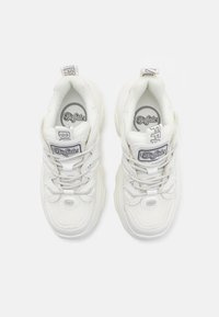 White sneakers with a textured mesh upper, round toe, chunky sole, and reflective accents. Features a logo patch on the tongue and heel tabs.