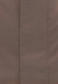 Καφέ ύφασμα με ομαλή υφή, που παρουσιάζει διακριτικές παραλλαγές στο χρώμα. Δύο κάθετες ραφές διατρέχουν το κέντρο.