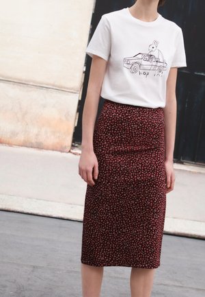Vrouw die een wit t-shirt draagt met een tekening van een auto en een konijn en de tekst "hop in!", gecombineerd met een donker bloemen midi-rok met een hoge taille.