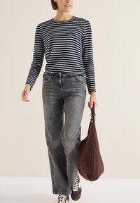 Top de manga larga a rayas en azul marino y blanco, combinado con vaqueros de pierna ancha grises y un bolso marrón oscuro de estilo desestructurado. Zapatillas marrones completan el conjunto.