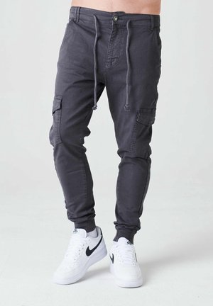 Pantalons cargo gris charbon avec taille à cordon de serrage, poches latérales, jambes fuselées et matériau en mélange de coton, associés à des baskets blanches.