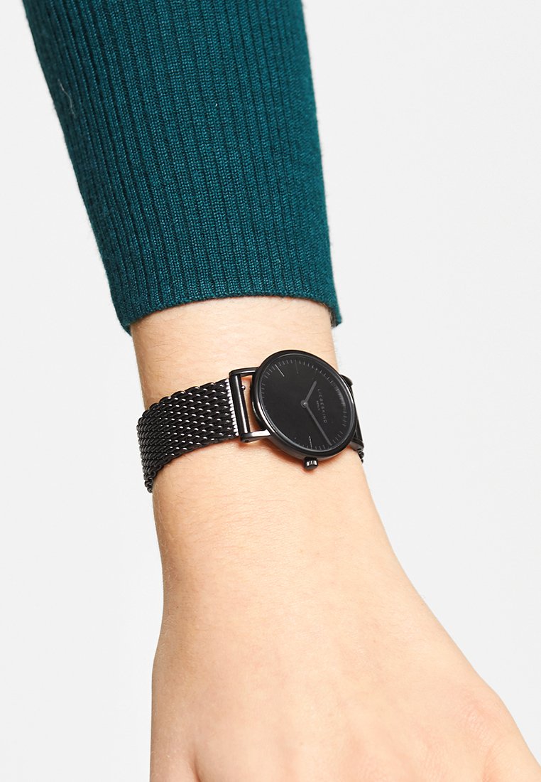 Zwarte polshorloge met een ronde wijzerplaat en een minimalistisch ontwerp. Beschikt over een gevlochten metalen band en een matte afwerking op de wijzerplaat.