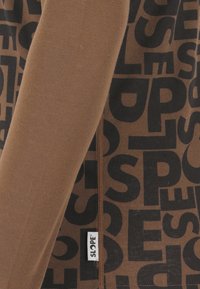 Brauner Langarmoberteil mit großen schwarzen Textmustern, gerippter Textur und einem seitlichen Etikett mit der Aufschrift "SLOPE."