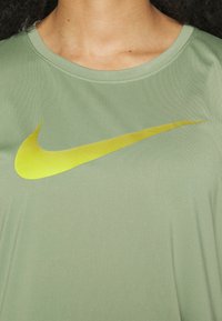 Ljust grön kortärmad skjorta i mjukt tyg med en framträdande gul Nike-logotyp över framsidan och rund halsringning.