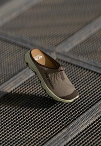 Lys brun slip-on sko med teksturert overdel og mørk brun tåhette. Lettvekts, gummiert såle i lys grønn med merkevarelogo. Usynlig snøring.