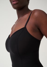 Body nero con scollatura a V profonda, spalline sottili e tessuto morbido ed elastico. La prospettiva ravvicinata evidenzia il design sagomato.