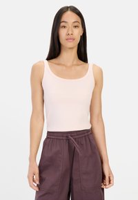 Pale pink sleeveless tank top with a scooped neckline, fitted design, and smooth texture, paired with loose-fitting dark purple cargo pants.
