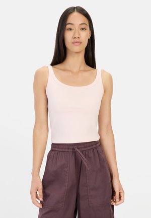 Pale pink sleeveless tank top with a scooped neckline, fitted design, and smooth texture, paired with loose-fitting dark purple cargo pants.