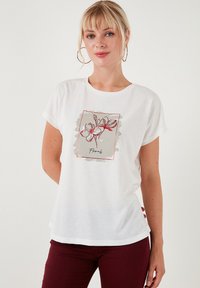 Witte katoenen t-shirt met een bloemenafbeelding in rood en grijs. Zachte textuur, relaxte pasvorm, met korte mouwen en een ronde halslijn.