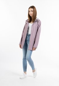 Chaqueta impermeable de color púrpura claro con capucha, cierre frontal con cremallera y botones a presión, combinada con jeans claros y zapatillas blancas.