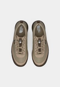 Beige sneakers with a textured fabric upper, brown laces, and rubber soles. Features logo detailing and a streamlined design.