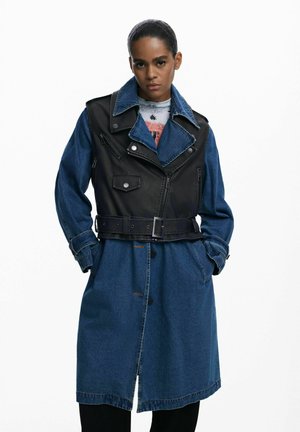 Abrigo trench de mezclilla negro y azul con cintura ceñida, grandes solapas, cierre delantero con cremallera, múltiples bolsillos y detalles de costura contrastantes.
