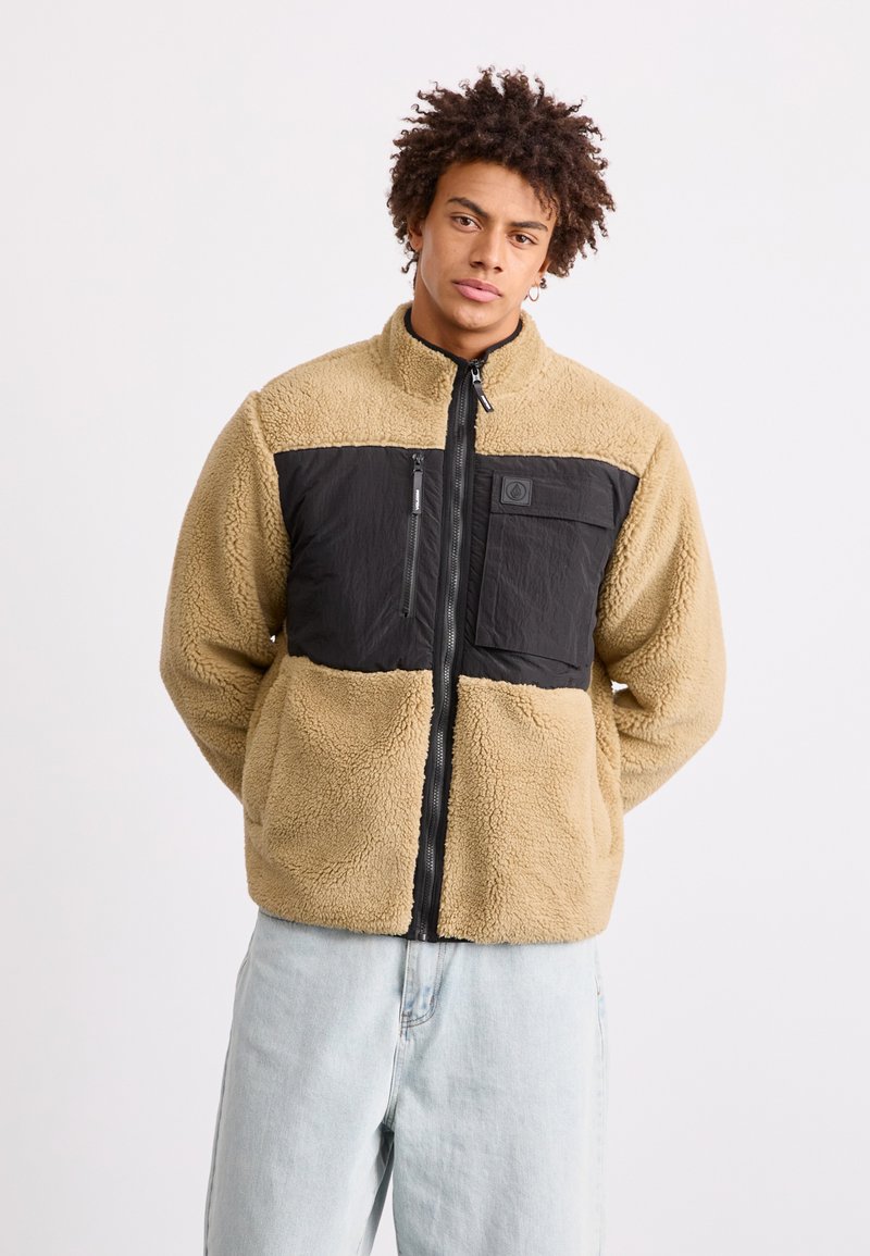 Tarn- und schwarze Fleecejacke mit hohem Kragen, Reißverschluss und einer Brusttasche; weiche Textur mit kontrastierenden Paneelen.