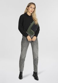 Camisa negra de manga larga, Jeans grises desgastados y botines. El modelo lleva un bolso mensajero verde y azul marino, con costuras en contraste.