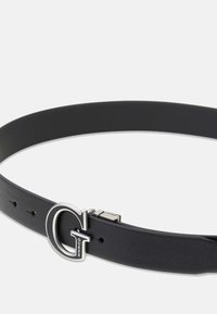Ceinture en cuir noir avec une surface texturée et une boucle argentée en forme de « G » avec le nom de la marque « Guess » en dessous. Taille ajustable.
