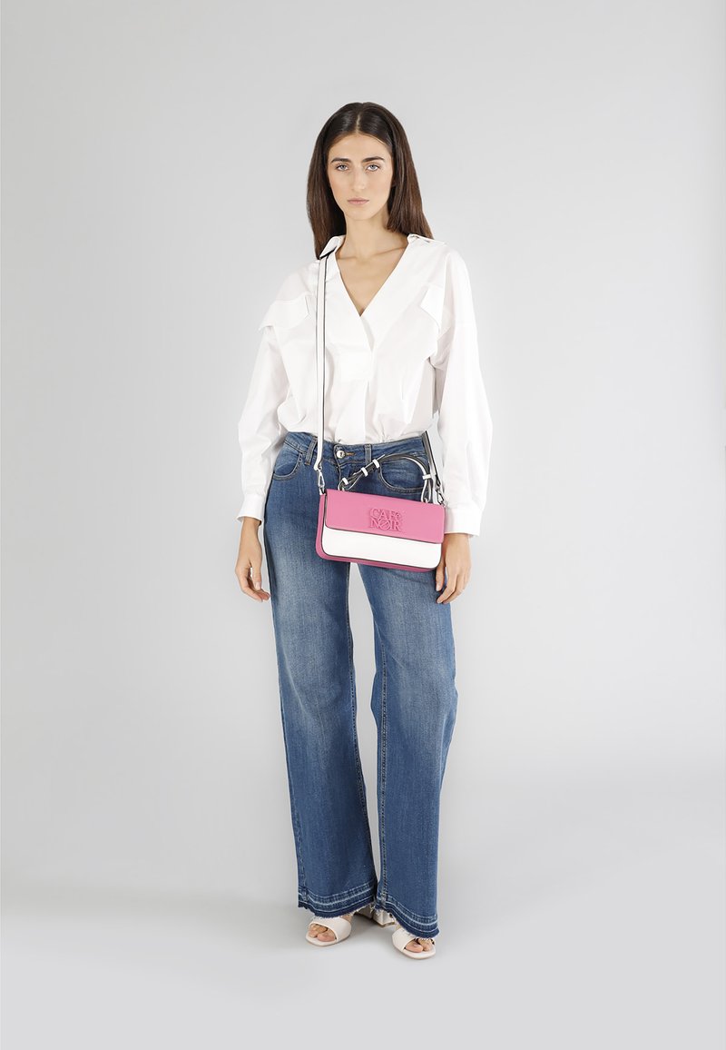 Blusa bianca a maniche lunghe, jeans a gamba larga blu e una borsa strutturata rosa e bianca con logo. Il modello indossa tacchi di colore chiaro.