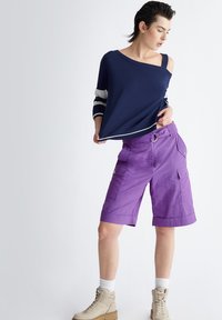 Top navy a spalle scoperte con maniche a righe e vestibilità ampia, abbinato a pantaloni cargo viola con tasche a toppa e dettaglio per il passante della cintura.