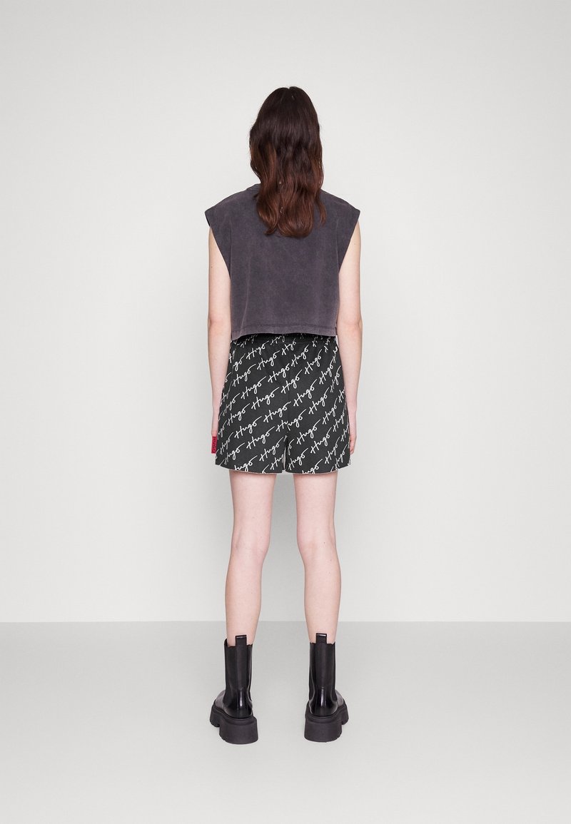 Haut sans manches gris à coupe décontractée, associé à une jupe noire à motifs avec du texte blanc, complété par des bottes noires arrivant au mollet.