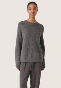 Grå strikket sweater med en blød tekstur, rund hals og lange ærmer, parret med grå bukser med striber.
