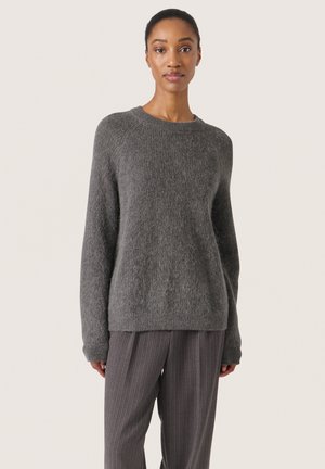 Gray knitted sweater with a soft texture, crew neck, and long sleeves, paired with pinstriped gray trousers.