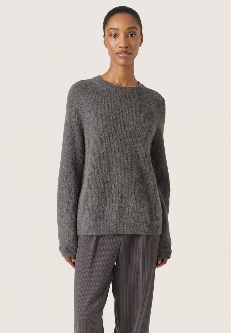 Grå strikket sweater med en blød tekstur, rund hals og lange ærmer, parret med grå bukser med striber.