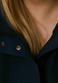 Námořnická modrá bunda se zipovým zapínáním, stříbrným kováním a kapucí, s texturovanou tkaninou a viditelnými švy.