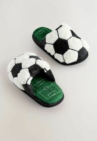 Sort-hvide fodbold-inspirerede slippers med en blød overflade, der har en grøn indersål designet som en fodboldbane.