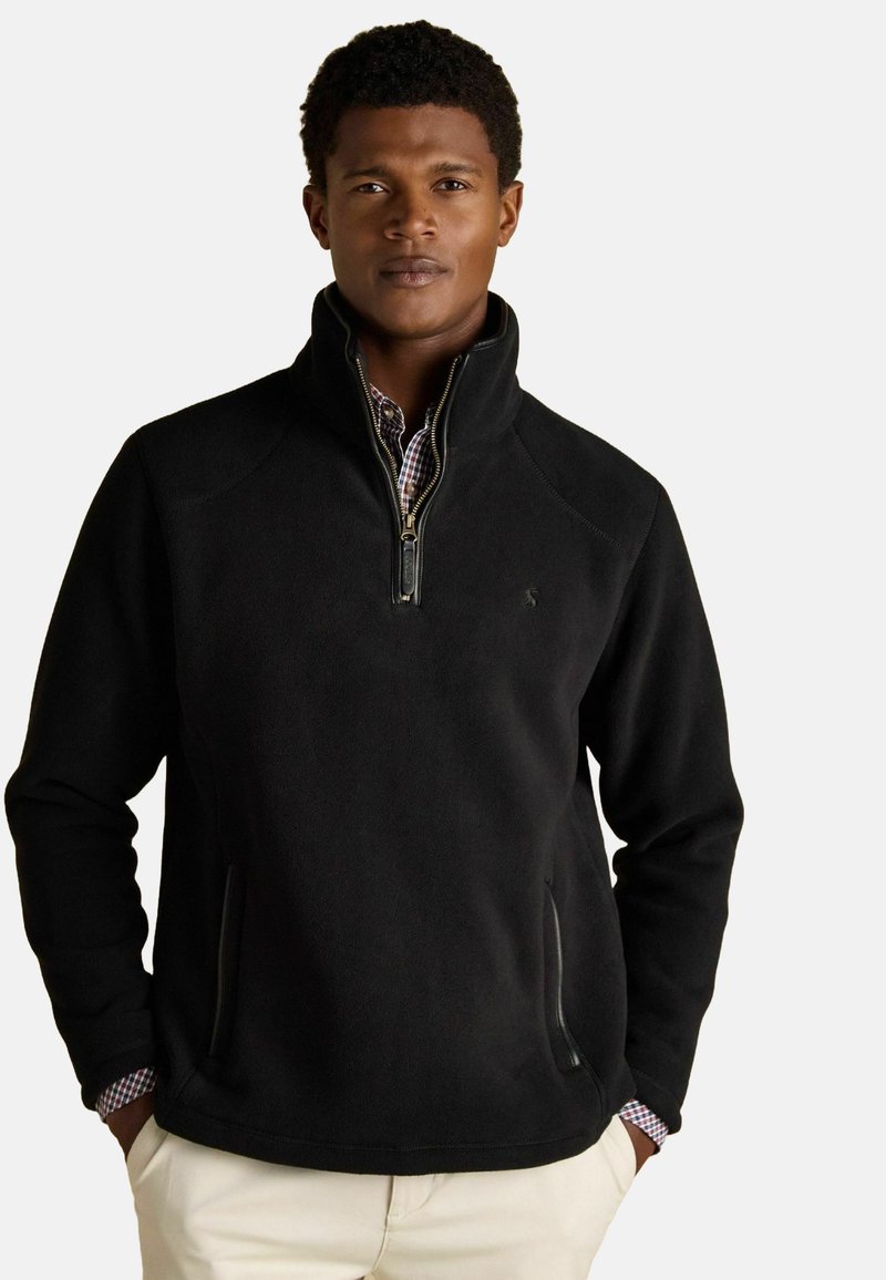 Pullover in felpa nera con colletto a metà zip, tasche laterali e fodera a quadri contrastante visibile ai polsini, con un logo discreto.