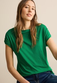 Grøn kortærmet t-shirt med en afslappet pasform, lavet af blødt stof, med sammenskrumpede detaljer på ærmerne og en simpel rund hals.