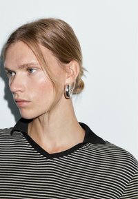 Striped shirt with a black collar, featuring white and black horizontal lines. Model wears silver hoop earrings. Smooth skin texture.