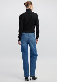 Schwarzer Strickrollkragenpullover mit verziertem Muster; kombiniert mit blauen, geraden Jeans mit Gesäßtaschen und fransigem Saum.