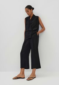 Black sleeveless top and wide-leg pants in a smooth fabric, featuring a draped design. Paired with black flip-flops. Minimalist modern look.