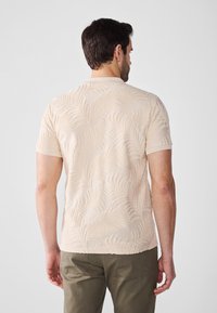 Beige színű, rövid ujjú ing, textúrált pálmalevél mintával. Az anyag lágy tapintású, sima felületű és enyhén szűkített fazonú.