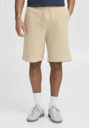 Pantalones cortos de color beige, hasta la rodilla, hechos de una tela texturizada con un patrón de cuadrícula. Cuentan con una cintura elástica con cordón y bolsillos laterales.