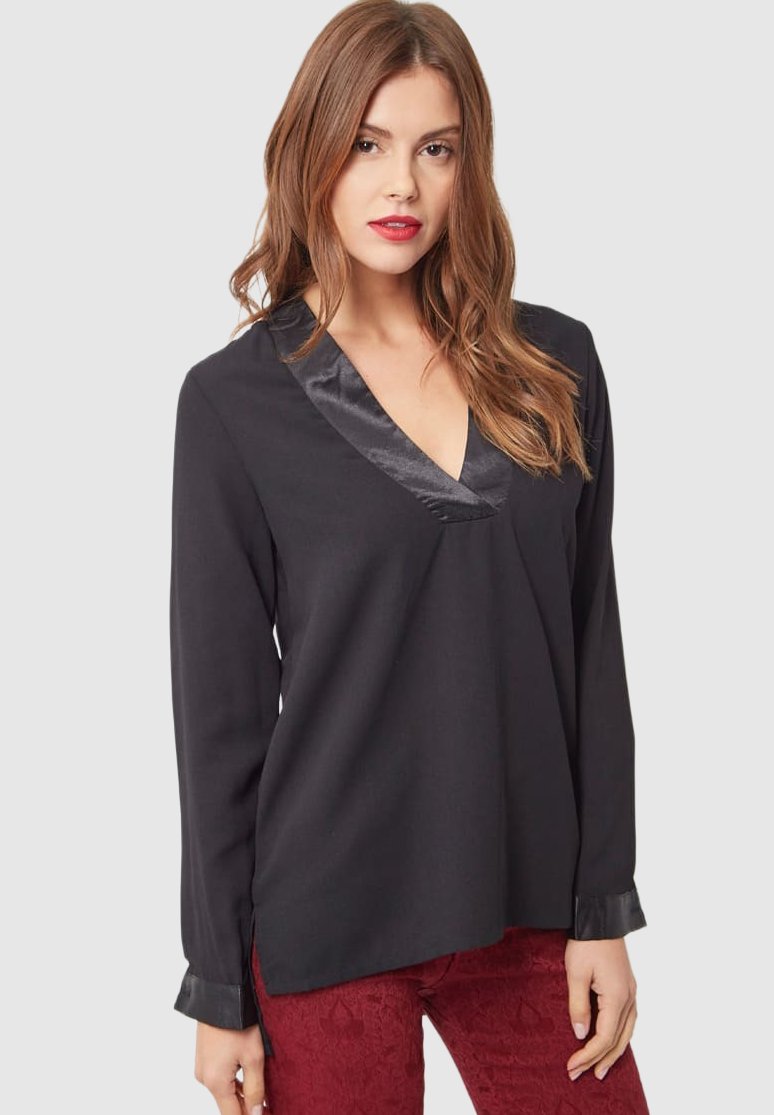 Camisa negra de manga larga con un cuello en V de satén, textura suave y detalles en los puños, combinada con pantalones rojos con estampado.