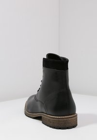 Mustat nahka-nilkkurit, joissa on nauhakiinnitys, turkistasku, puukorko ja teksturoitu kumipohja. Sujuva viimeistely, jossa on kaarevat muodot.