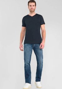 Camiseta negra de pico combinada con jeans azules claros, con corte recto y lavado claro. Complementada con zapatillas blancas.